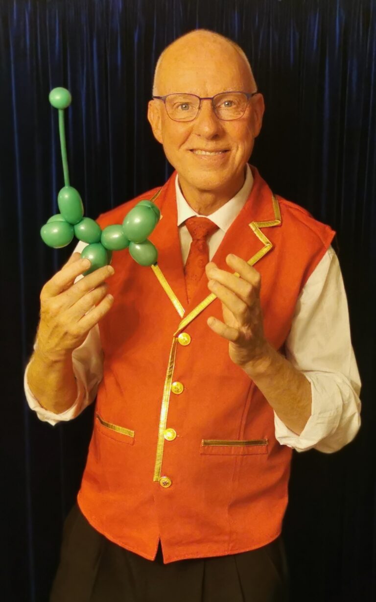 Tryllekunstner Ole Larsen i rød vest med en grøn ballonhund i hånden skaber magiske øjeblikke for børn og voksne